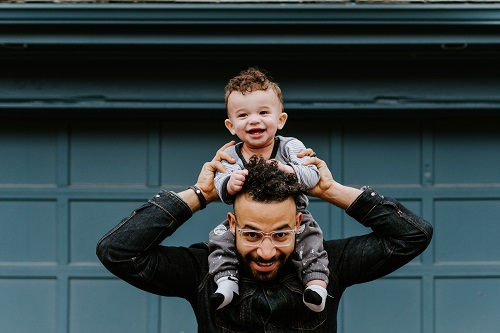 a man carries a smiling toddler on his shoulders